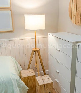 pés de uma cama com duas cómodas altas no fundo, um candeeiro de pé e dois bancos de madeira maciça